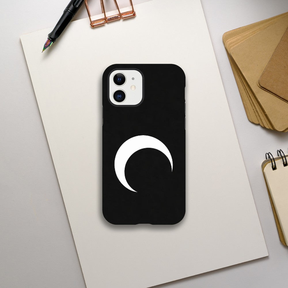 Black phone case with a white crescent moon design on a light gray surface with stationery items.