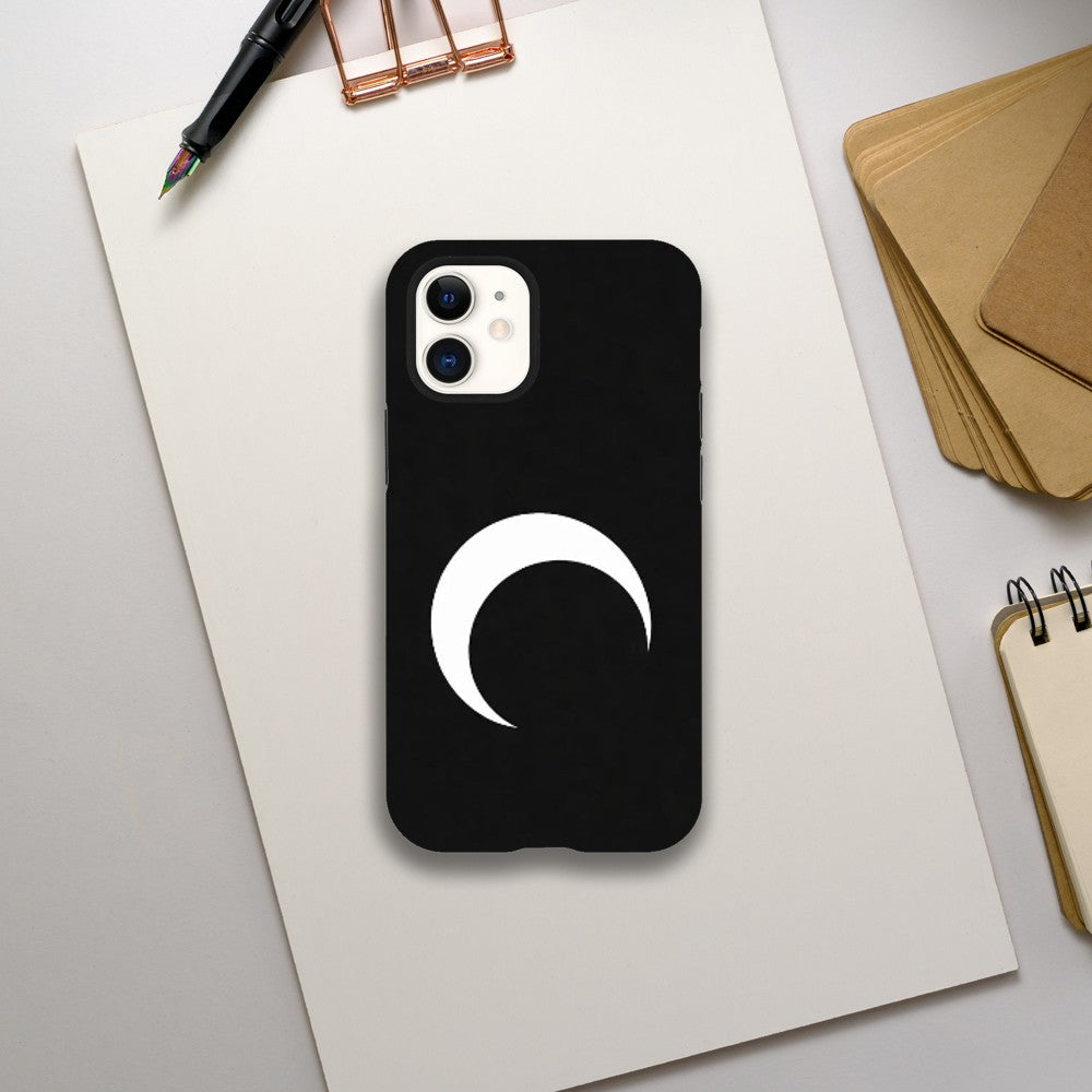 Black phone case with a white crescent moon design on a light gray surface with stationery items.