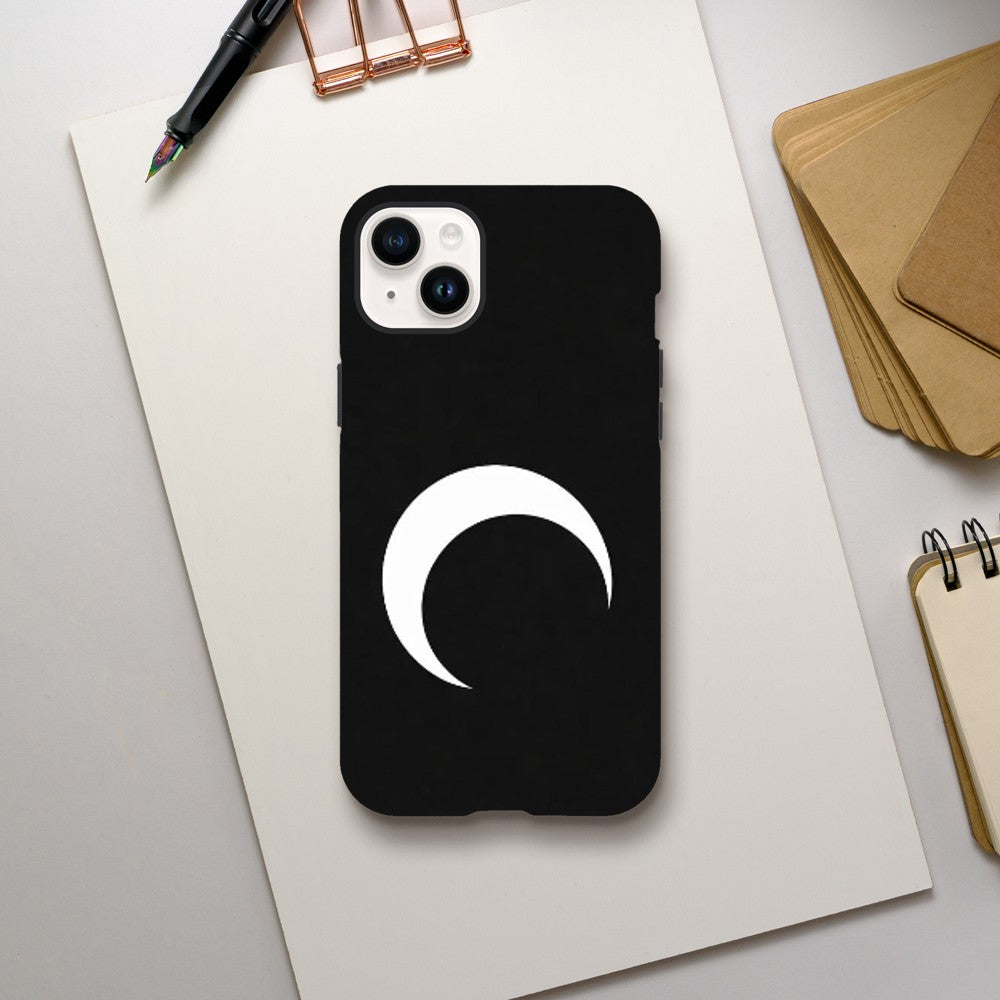 Black phone case with a white crescent moon design on a light gray surface with office supplies.