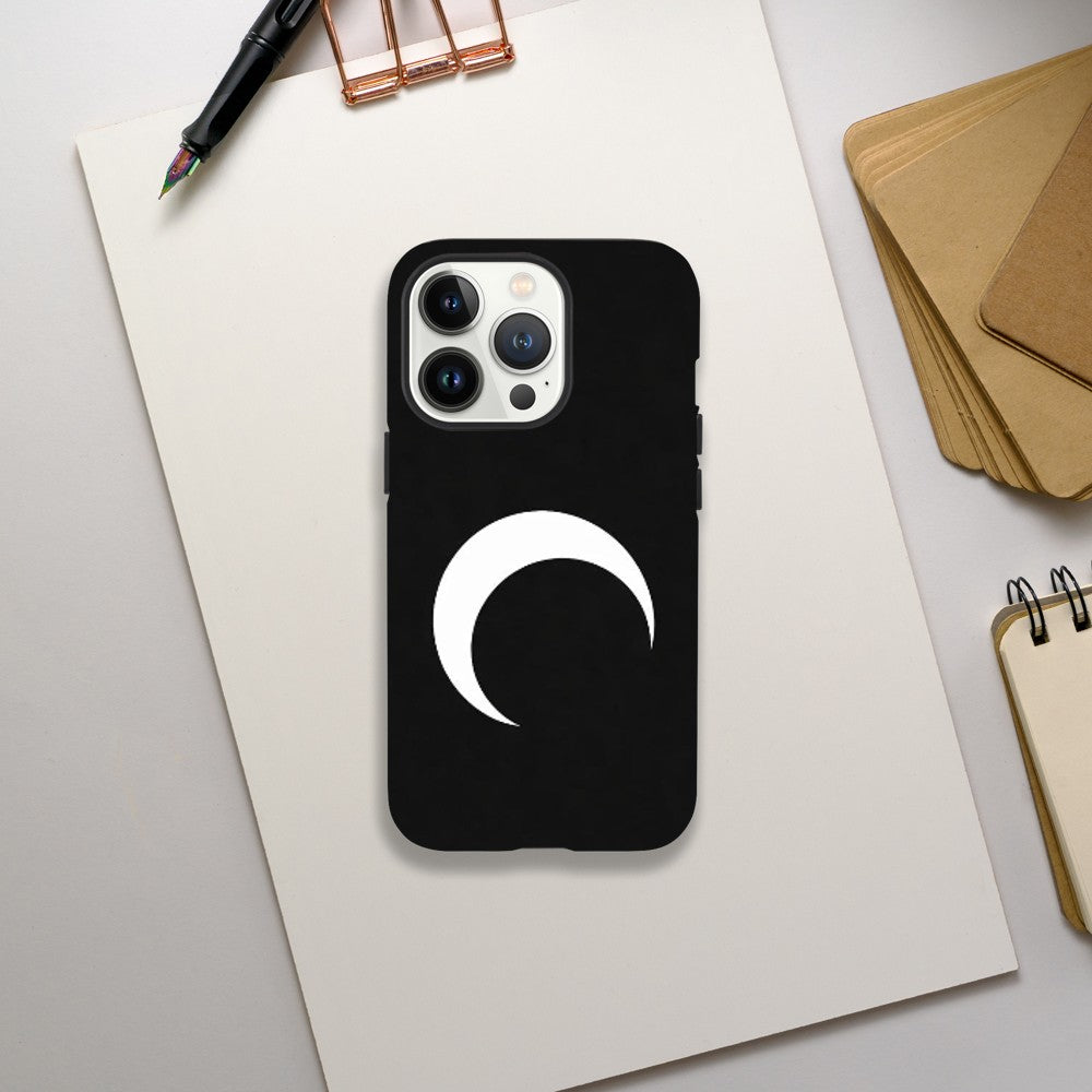 Black phone case with a white crescent moon design on a light gray surface with office supplies.