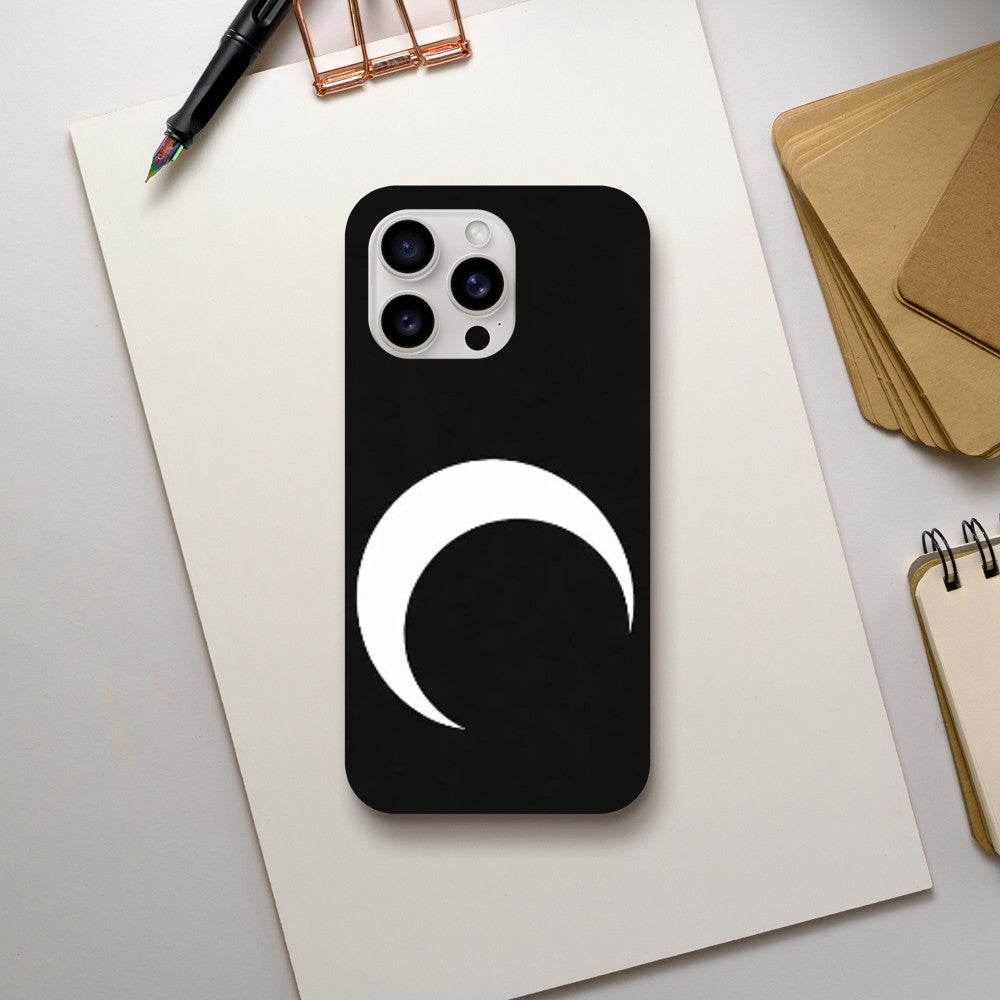 Black phone case with a white crescent moon design on a light gray surface with office supplies.