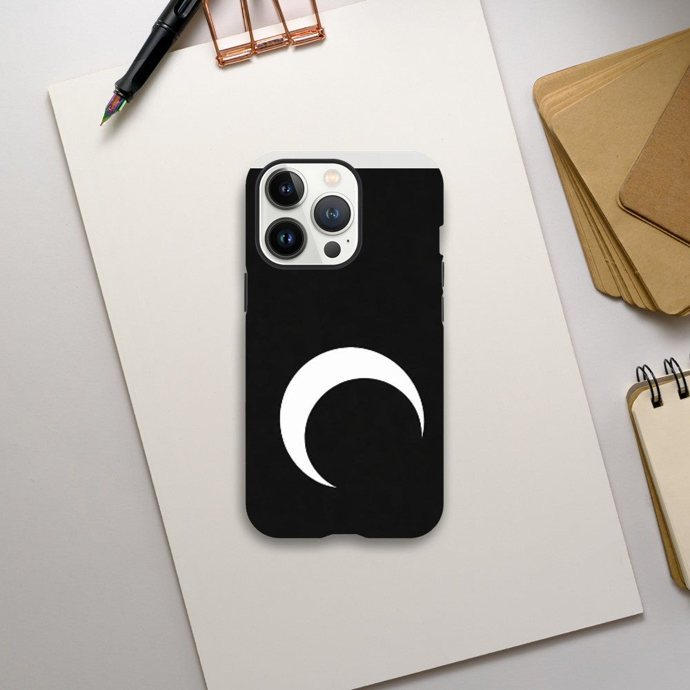 Black phone case with a white crescent moon design on a light gray surface with stationery items.