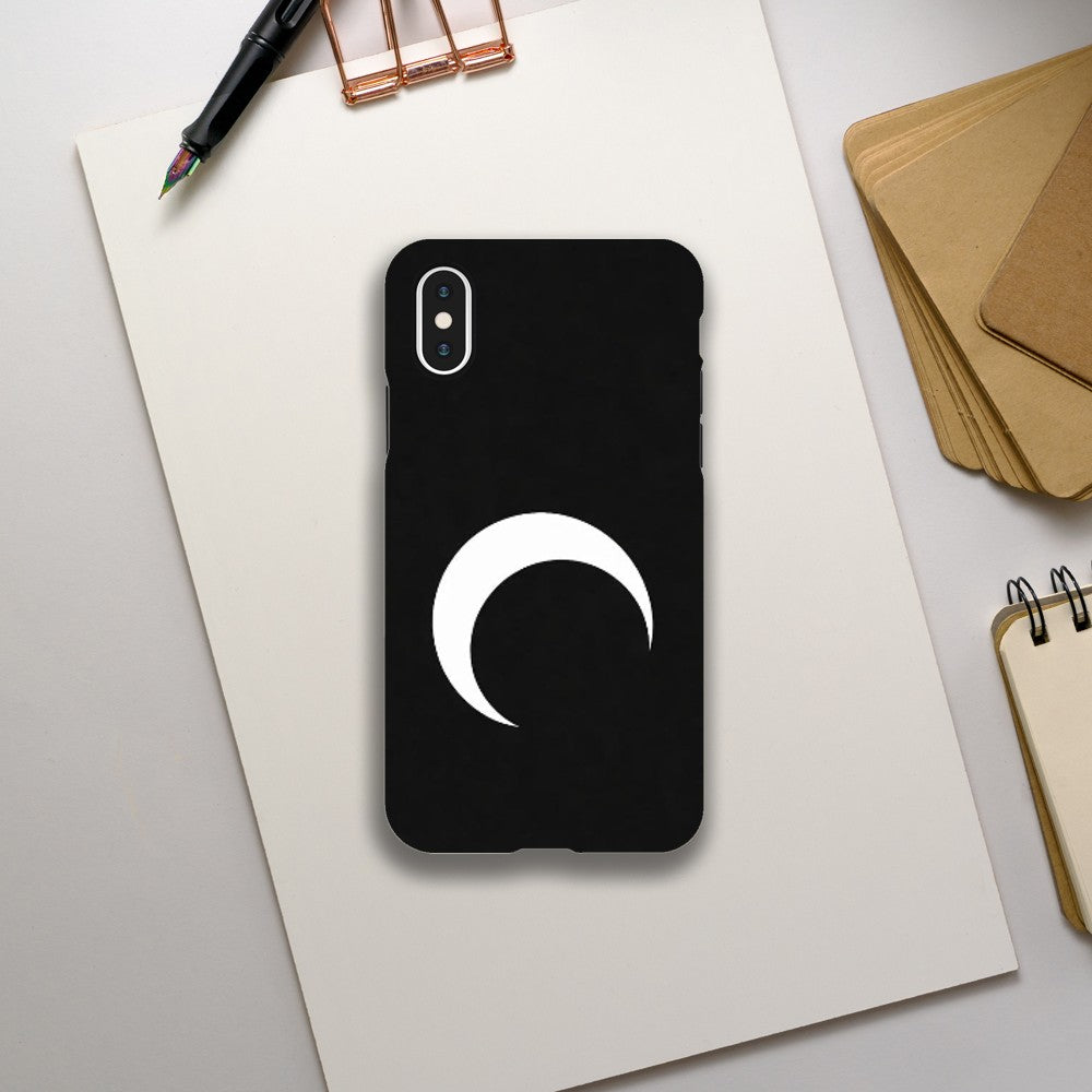 Black phone case with a white crescent moon design on a light gray surface with stationery items.