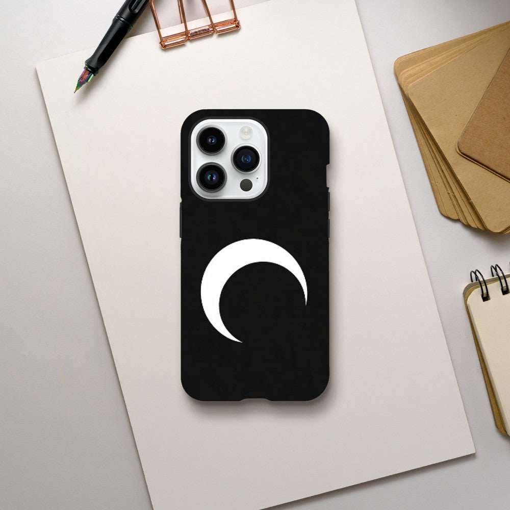 Black phone case with a white crescent moon design on a light gray surface with office supplies.