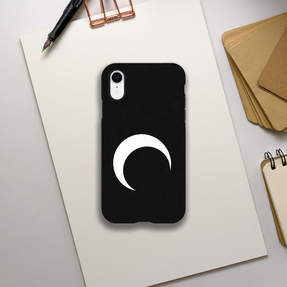 Black phone case with a white crescent moon design on a light gray surface with stationery items.